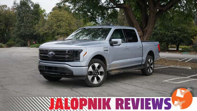 A silver 2023 Ford F-150 Lightning is parked in front of a large tree