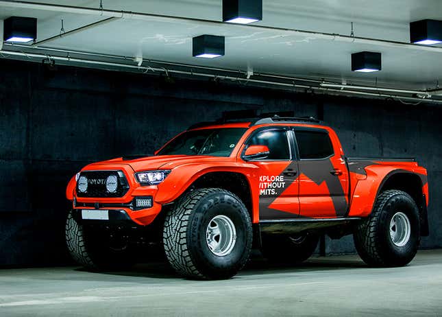 A red and gray liveried Toyota truck with massive tires is parked in a warehouse.